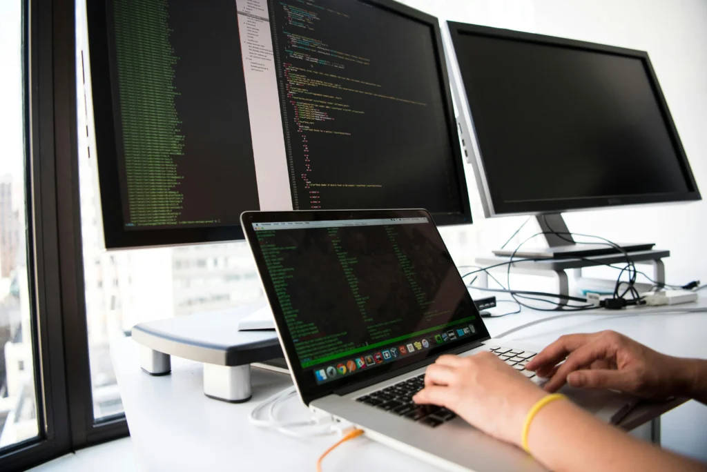 電腦供電設備A developer writes code on a laptop in front of multiple monitors in an office setting.