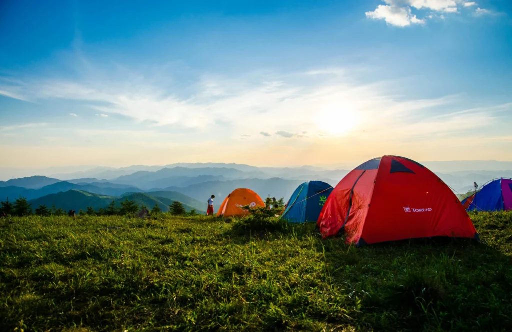 露營區場地Vibrant tents on a grassy mountain ridge with a stunning sunrise view, ideal for adventure.